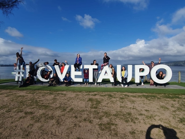 Large group posing with a big hashtag sign beside a lake.
