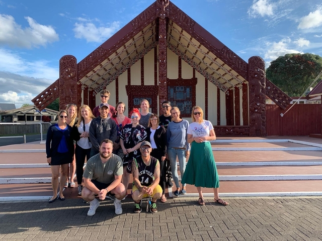 Group of people in front of a traditional Maori meeting house.