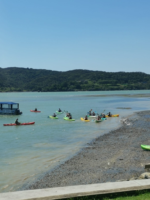 People kayaking on a blue lagoon with hills in the background.