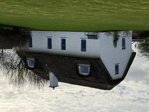       Charming white thatched-roof cottage with blue windows set on a green lawn.
  