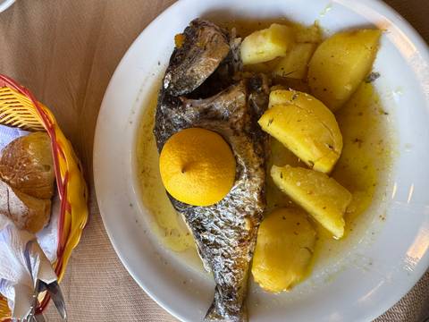       Plate of roasted fish with potatoes topped by a whole lemon in a Greek taverna.
  