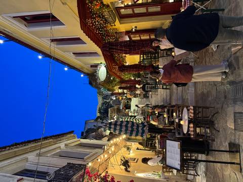       Bustling stepped alley in Athens’ Plaka district lined with cafés and diners at blue twilight.
  