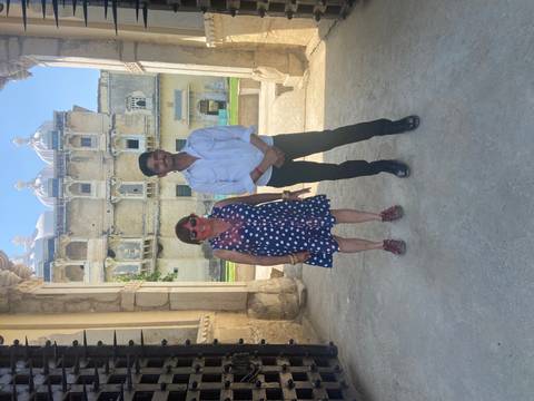       Two people standing in the courtyard of an old palace building with weathered walls and arches.
  