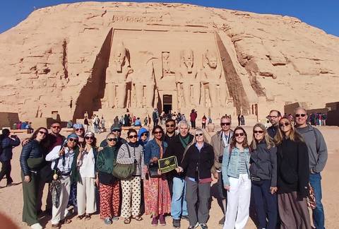       Large tour group posing in front of the colossal statues of Abu Simbel temple.
  