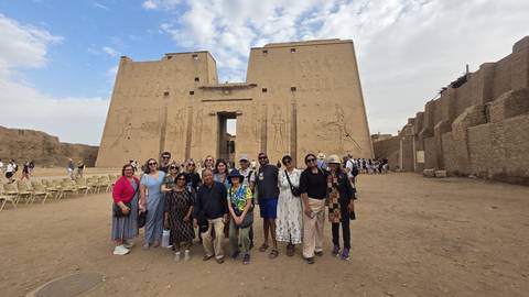       Large tour group poses in front of an ancient Egyptian temple with towering sandstone walls
  