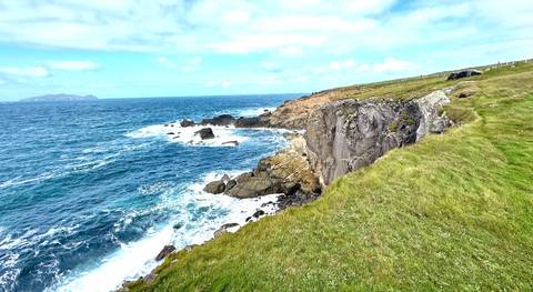       Wind-swept Atlantic cliffs with turquoise waves crashing below under a bright sky.
  
