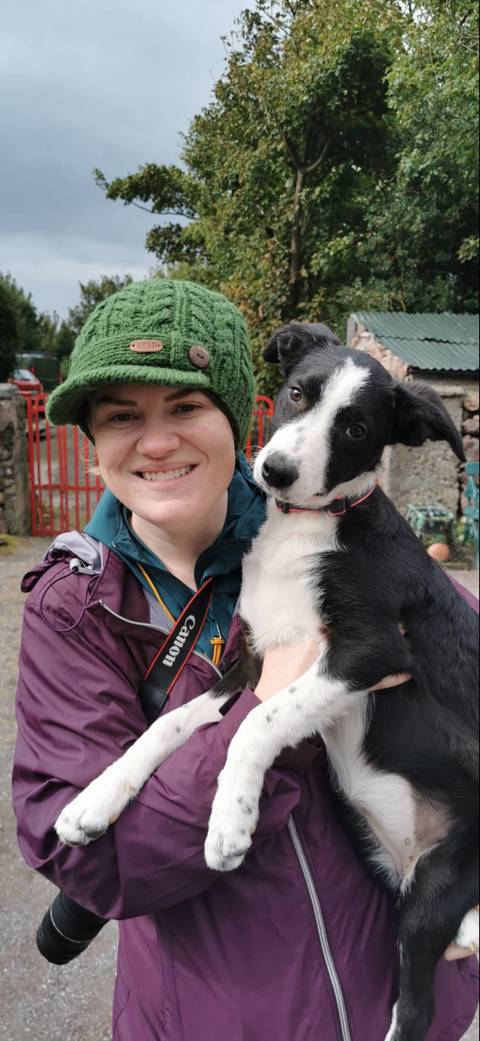       Close-up portrait of a smiling traveller holding a black-and-white dog.
  