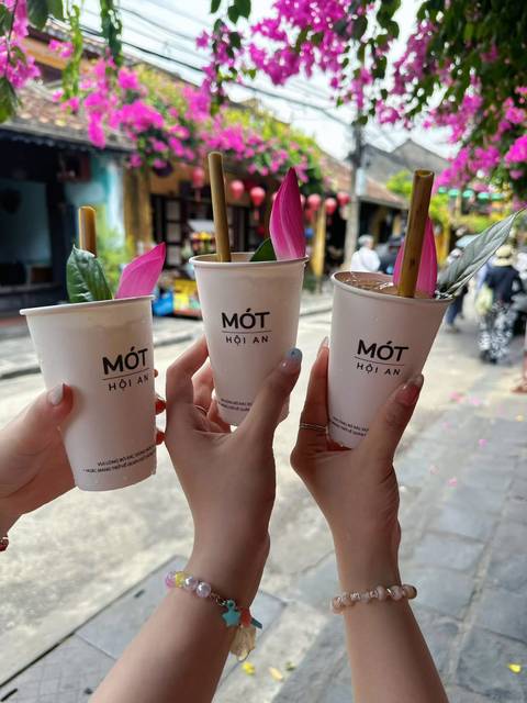       Three hands toast with signature Mót Hoi An herbal drinks on an old-town street.
  