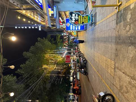       Night street scene with festive fairy lights, scooters parked and a lone pedestrian.
  