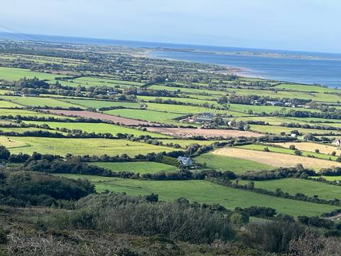      Expansive rural patchwork of fields leading to a distant coastline under blue skies.
  