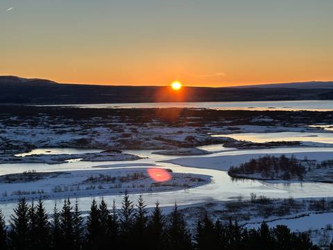       Winter sunset over snowy lakes and winding rivers with the golden sun just above the horizon
  