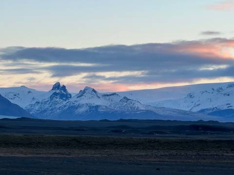       Snow-clad jagged peaks under pastel evening clouds above a dark volcanic plain
  