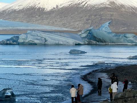       Tourists viewing massive blue icebergs along a frozen shoreline under a cloudy sky
  
