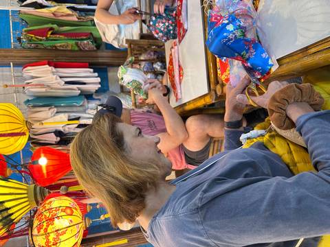       Travelers crafting colorful lanterns at a wooden table inside a bustling Vietnamese market stall
  