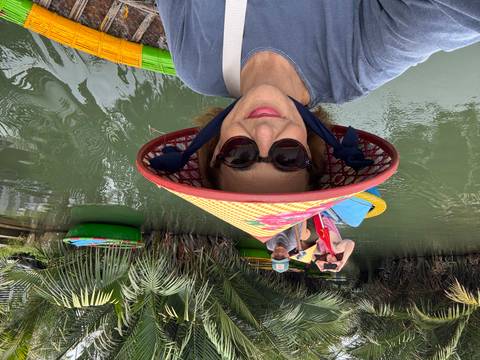       Selfie of woman in conical hat riding a colorful basket boat through lush nipa palm waterways
  