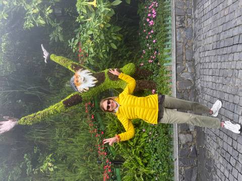       Smiling woman posing beside a moss-covered monkey topiary sculpture with arms raised in a misty garden
  