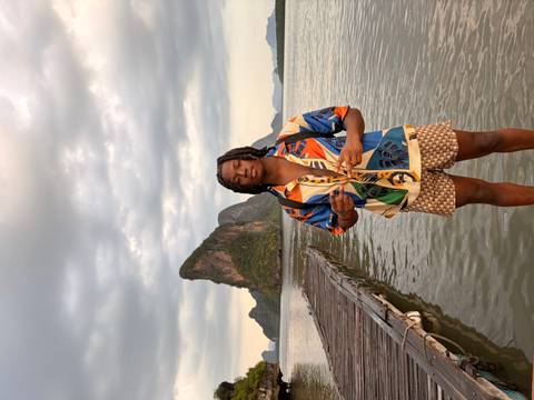       Man poses on a wooden pier with a dramatic limestone pinnacle and overcast sky beyond calm water.
  