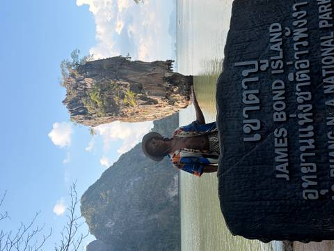       Visitor stands before the iconic karst of James Bond Island holding a welcoming gesture.
  