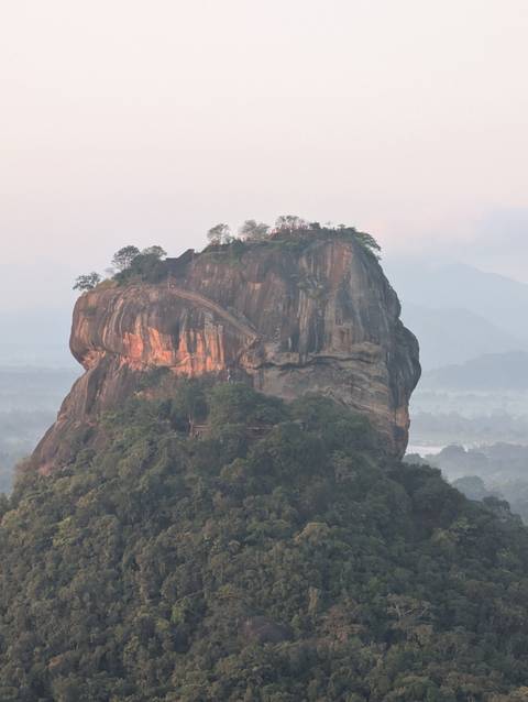       The iconic Sigiriya rock fortress rising above the surrounding jungle in soft sunrise light
  