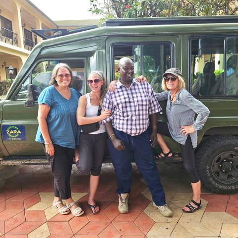       Travellers posing with safari driver beside a green 4x4 vehicle
  