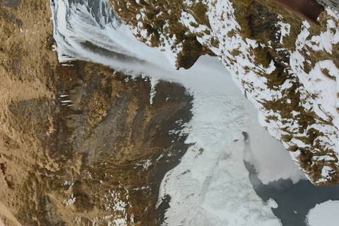       Tall waterfall plunging into a partially frozen canyon with snow and icicles along rocky cliffs.
  