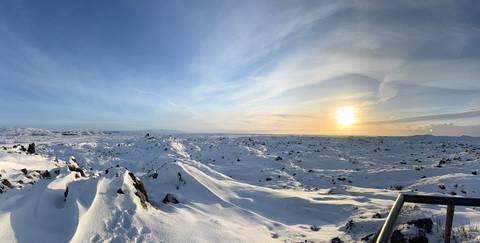       Vast snow-covered lava field bathed in low sun, stretching toward the horizon under a blue sky.
  