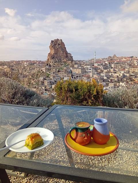       Breakfast table set on a terrace facing Ortahisar’s towering rock castle and surrounding townscape.
  