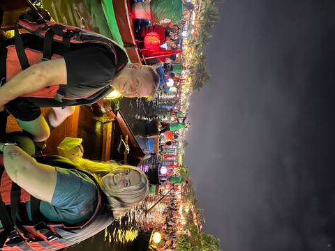       Two tourists seated in a lantern-lit boat among many colorful boats on a night river festival
  
