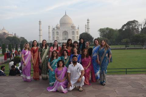       Group dressed in colorful saris posing in front of the Taj Mahal gardens
  