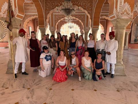       Tour group with palace guards inside an ornately decorated hall with arches in Jaipur
  