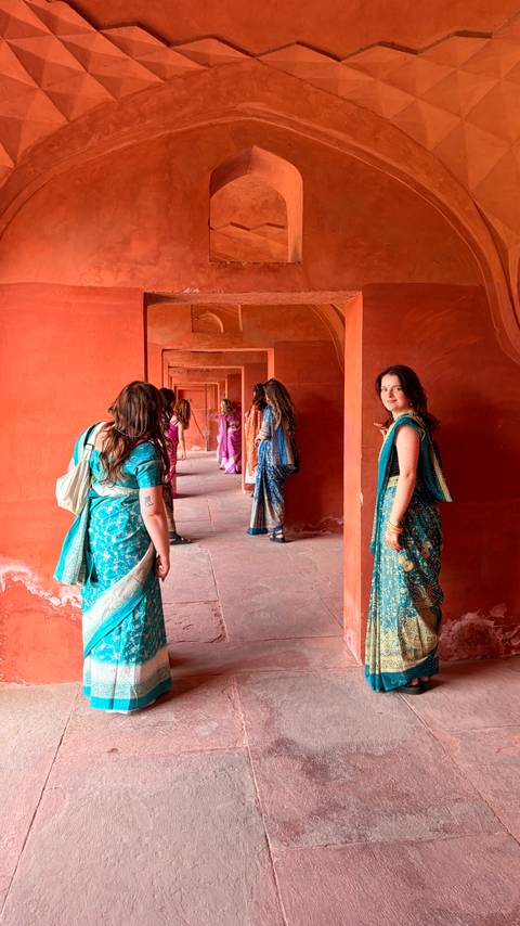       Women in colourful saris walking through a red sandstone corridor of an Indian fort.
  