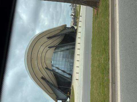       Curved modern glass and steel building photographed from inside a moving vehicle on cloudy day.
  