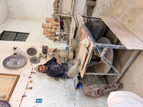       Potter shaping clay on a wheel inside a ceramics workshop surrounded by finished pots.
  