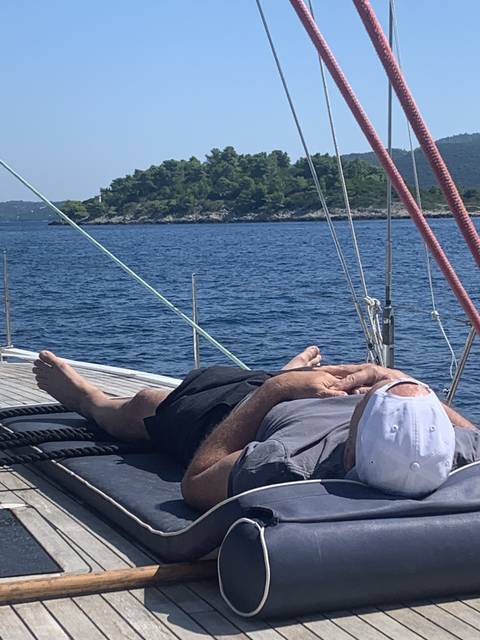       Man relaxing on a boat deck with a coastal view.
  