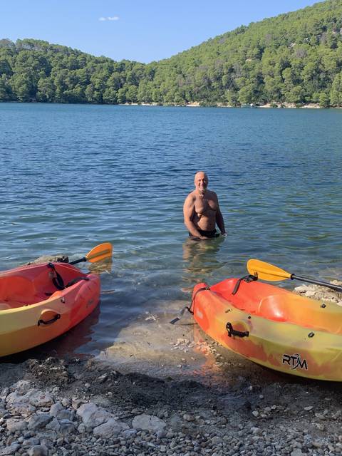 Man standing in shallow water next to colorful kayaks.