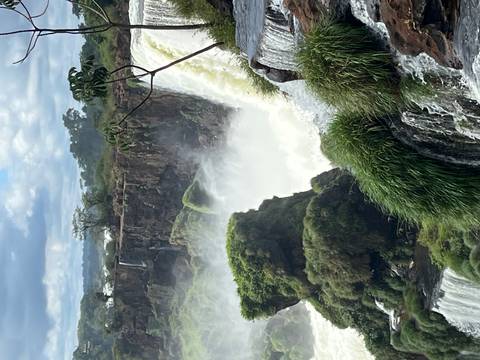       Thundering section of Iguazu Falls with mist rising and lush green moss-covered rocks.
  