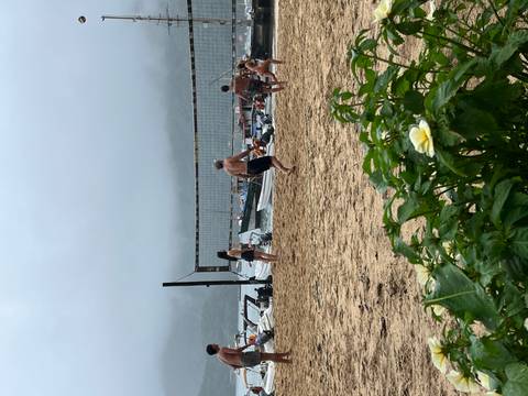       Young travellers playing beach volleyball on a foggy shore lined with boats.
  