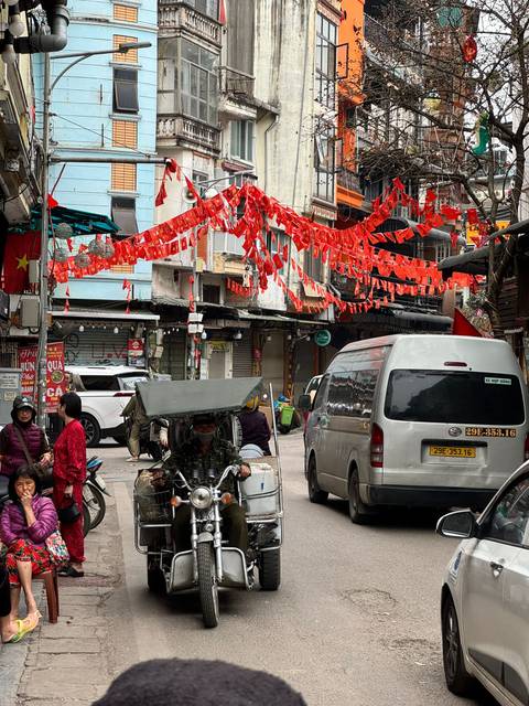       Bustling city street decorated with red lantern banners and motorbikes passing by.
  