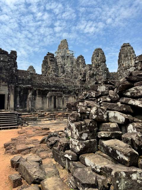       Ancient stone faces and crumbling walls of a temple complex surrounded by scattered blocks.
  