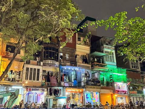       Nighttime view of narrow multi-story buildings illuminated with colorful lights and signage.
  