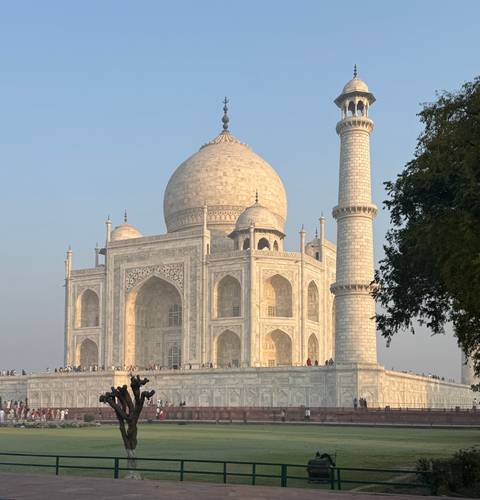       The Taj Mahal glowing in soft light with crowds walking along the platform.
  