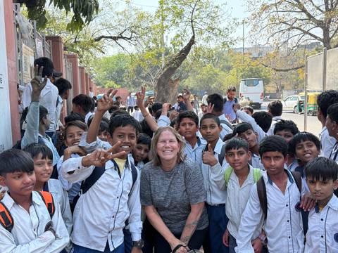       Smiling traveller surrounded by a large group of schoolchildren posing on a street.
  