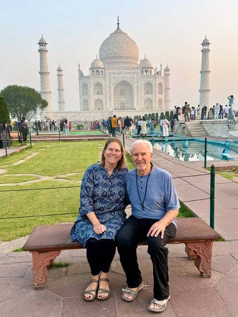       Couple seated on a bench with the Taj Mahal and reflecting pools in the background.
  