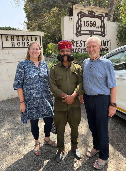       Travellers posing with a moustached local guide beside a white vehicle.
  