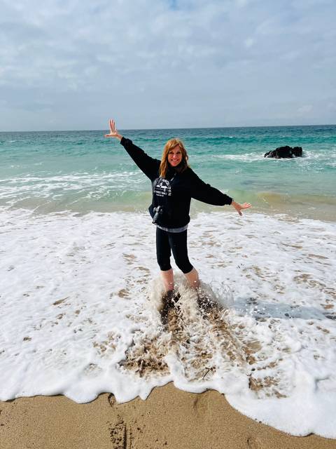       Woman splashes joyfully in shallow turquoise surf on a sandy beach.
  