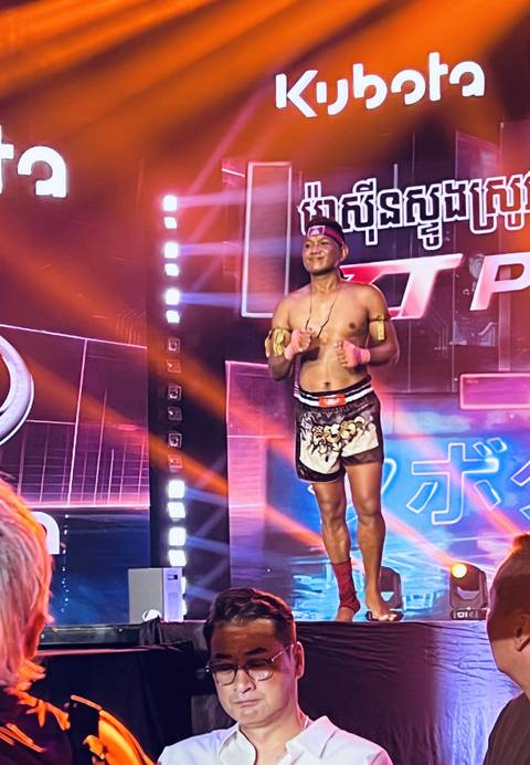      Muay Thai fighter on a brightly lit stage during an evening boxing show.
  