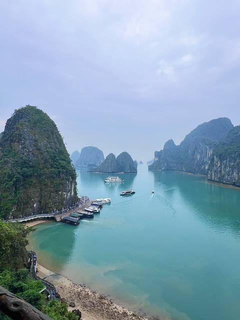       Emerald waters, limestone karsts and cruising boats in the misty expanse of Halong Bay.
  