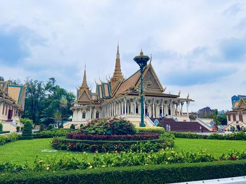       Ornate Royal Palace complex in Phnom Penh surrounded by lush gardens under a bright sky.
  