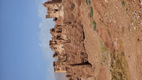       Crumbling earthen fortress walls stand isolated on arid rocky terrain beneath clear sky.
  