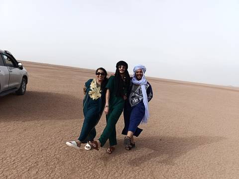       Three friends pose playfully on vast flat desert plain beside parked SUV.
  